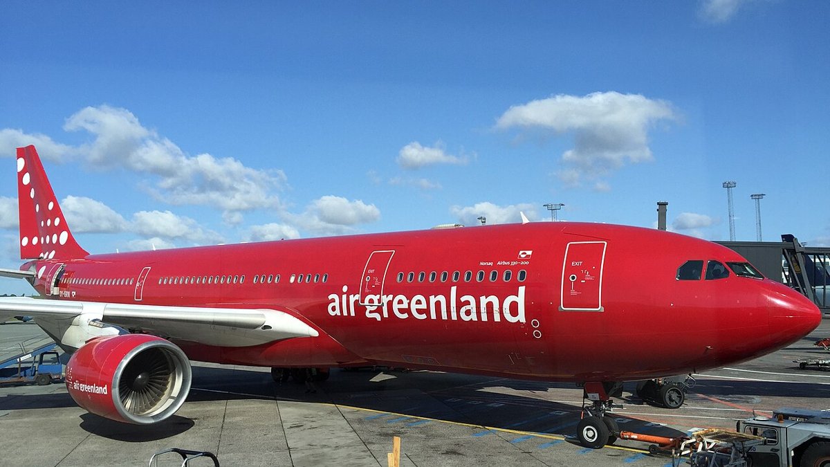 Et rødt Air Greenland Airbus A330-200 holder ved en gate i Københavns Lufthavn i solskin