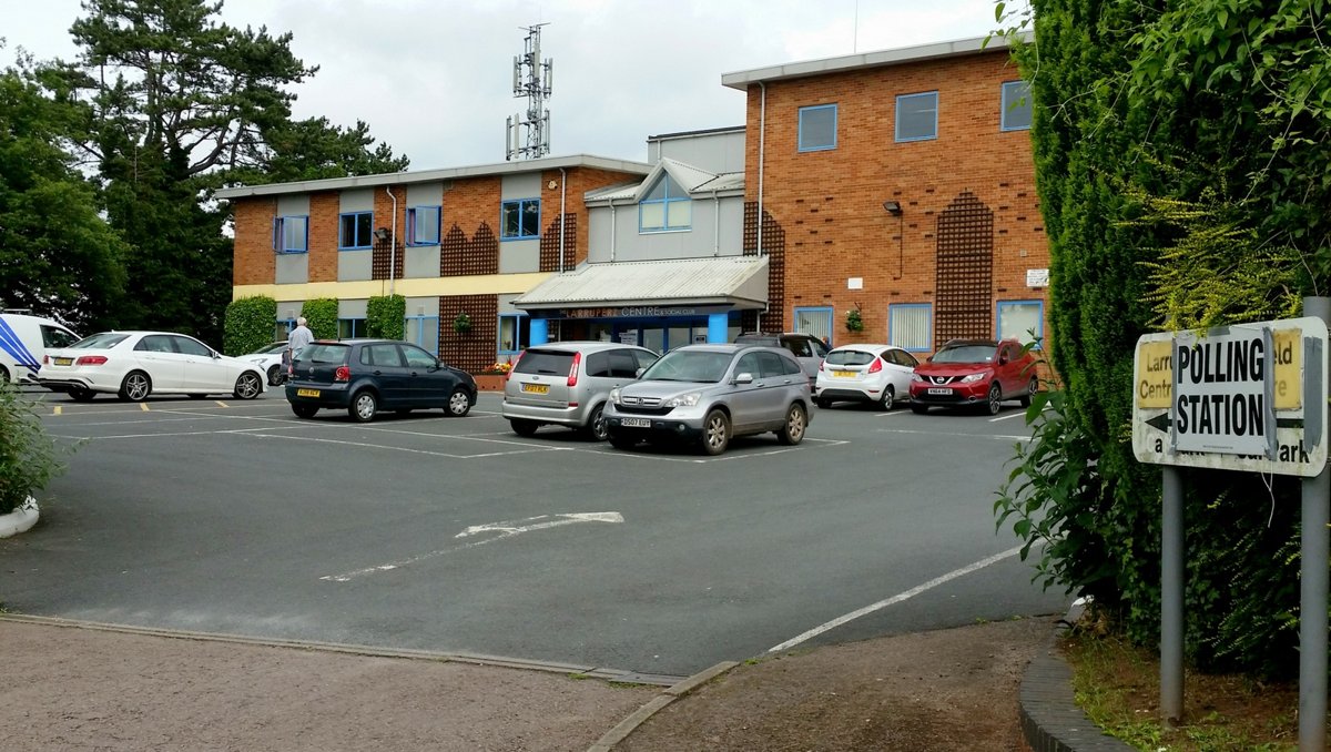 Skilt med teksten "Polling station" foran en kontorbygning med parkeringsplads i England