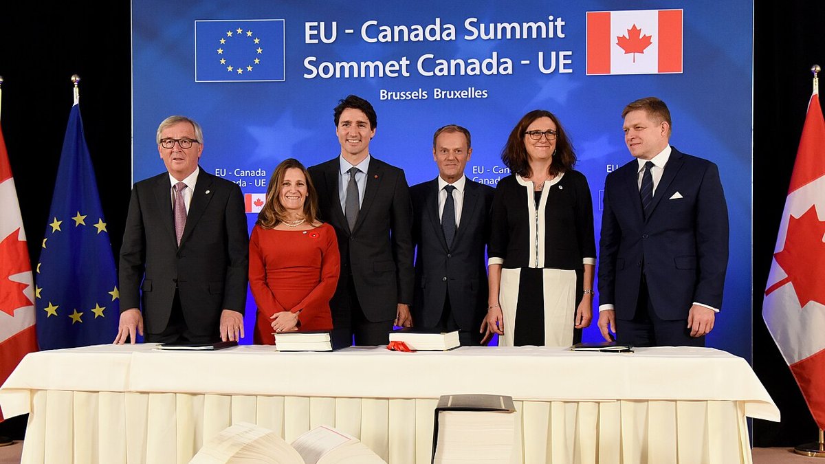 Seks politikere står bag et bord med de underskrevne aftaletekster foran et banner for EU-Canada-topmødet i Bruxelles