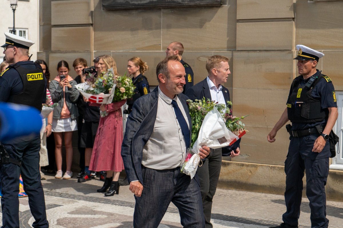 Martin Lidegaard i mørkt jakkesæt går med en buket blomster over Amalienborg Slotsplads, mens politibetjente og tilskuere står bag ham