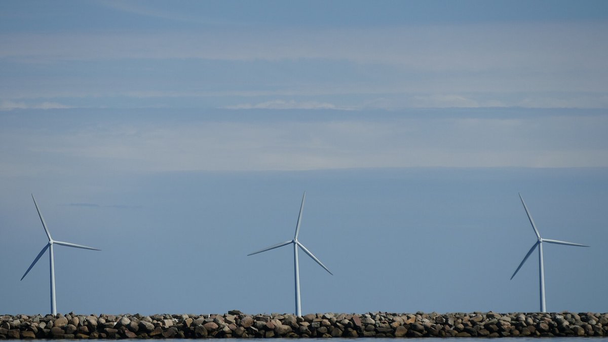 Tre vindmøller på en stensat mole i Øresund under en grå himmel
