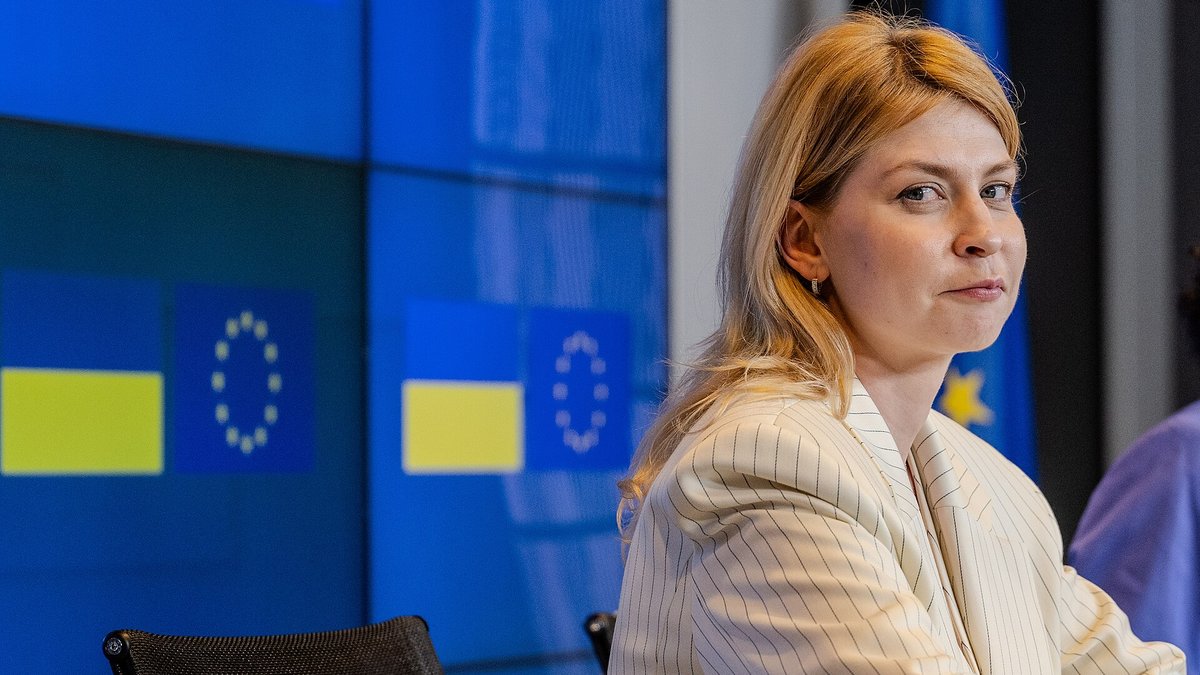 En deltager ved konferencebordet foran en skærmvæg med ukrainske flag og EU-flag